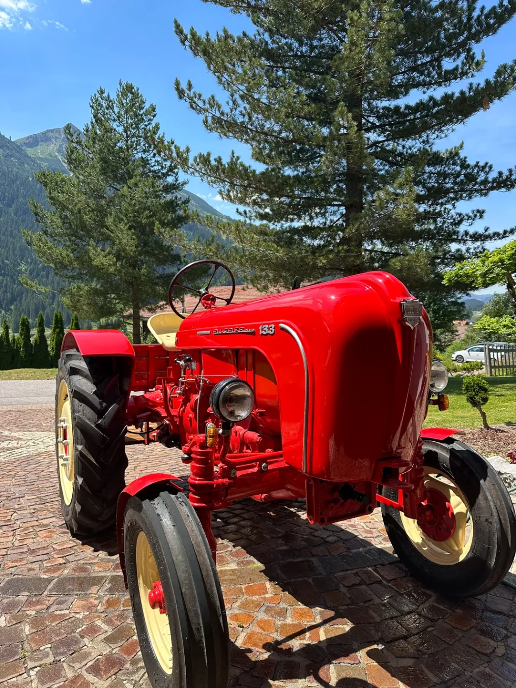 Roter Porsche-Diesel-Traktor vor dem Sunneschlössli mit Blick auf die Tannheimer Berge