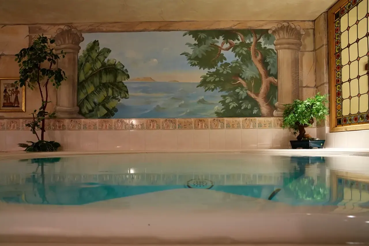 Der Whirlpool im Haus vor einer Wandmalerei mit Meer und Säulen, rechts ein Bleiglasfenster